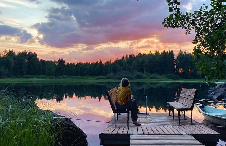 Donna guarda tramonto in Finlandia seduta su una panchina