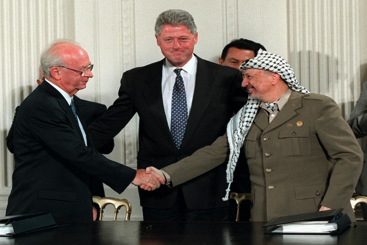 Yitzhak Rabin e Yasser Arafat (che indossa una kefiah) si stringono la mano davanti a Bill Clinton dopo la firma degli accordi di Oslo a Washington